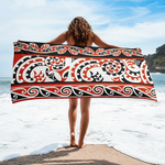 Person holding a large Maori beach towel with a tribal pattern on a beach.
