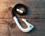 Hand carved Maori bone Hei Matau fish hook necklace with black adjustable cord, on a rustic wooden bench top