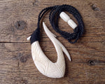 Hand-carved bone Hawaiian Makau fish hook necklace on a rustic wooden bench top