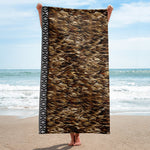 Person holding a Māori Kahu Huruhuru Beach Towel on a beach with ocean in the background