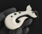 Hand-carved white cattle bone ocean talisman pendant resting upright in an open gloved hand, displaying the inner hook barb and graduated abalone shell discs.